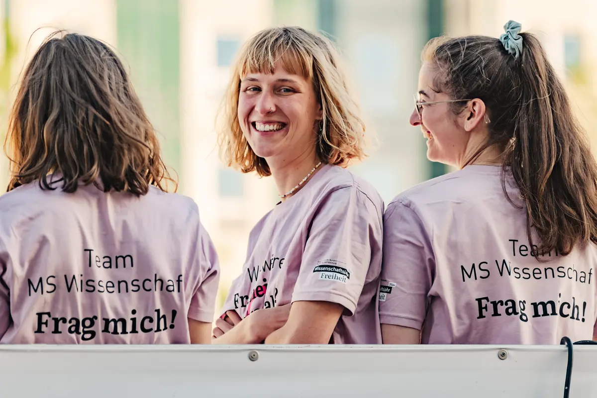 Drei junge Frauen in T-Shirts der MS Wissenschaft. Die eine Frau lacht in die Kamera.