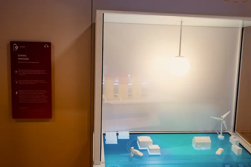 Das Bild zeigt ein Modell mit einzelnen Häusern, Elektroautos und einem Windrad.