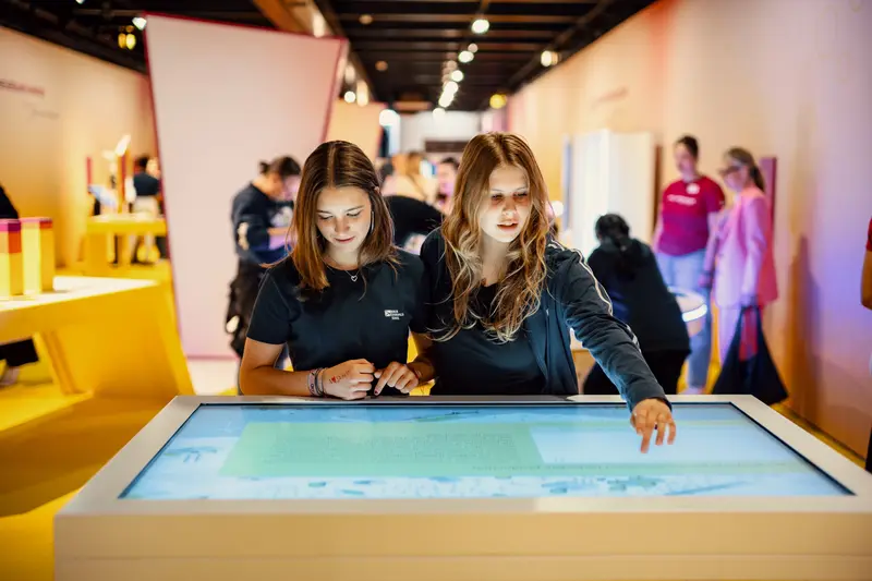 Zwei Schülerinnen bedienen einen großen Bildschirm.