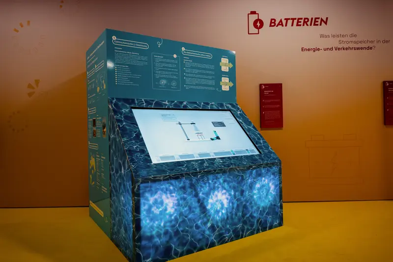 Das Bild zeigt ein großes blaues Exponat mit Informationstexten und einem Bildschirm.