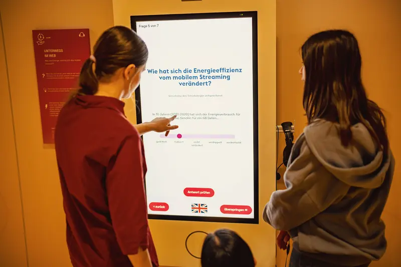 Das Bild zeigt zwei junge Frauen, die an einem großen Bildschirm ein Quiz zur Energieeffizienz des mobilen Internets machen.