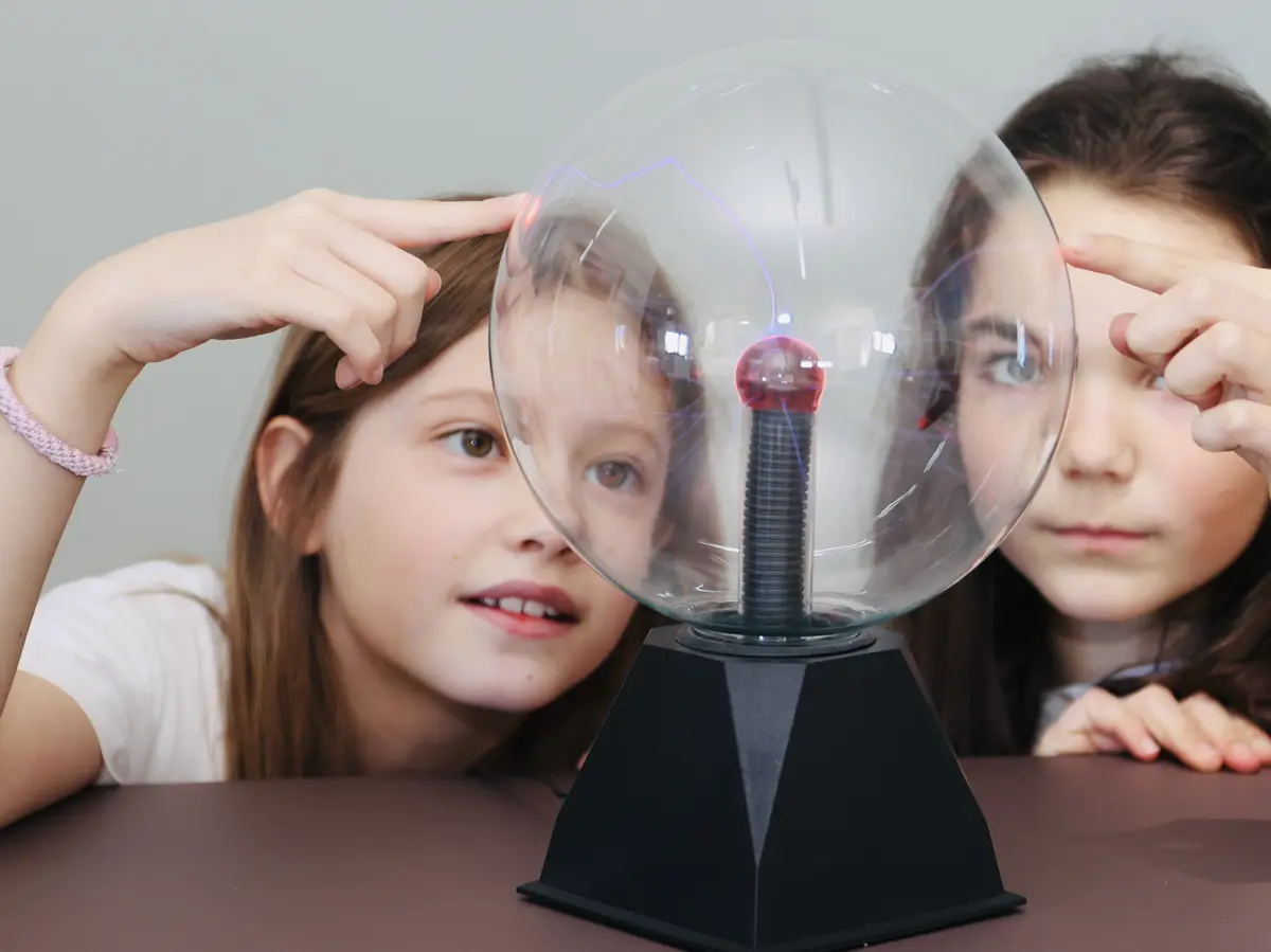 Zwei Kinder gucken eine Plasmakugel an.