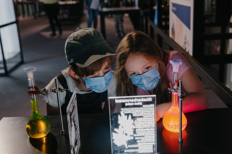 Zwei Kinder betrachten die fluoreszierenden Flaschen mit Wirkstoffen aus der Arzneimittelforschung.