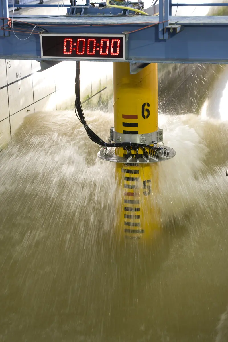 Eine gelbe Säule in einem Kanal mit einer großen Welle. Darüber eine Anzeige mit vielen Nullen. Auf der Säule eine Skala auf der die Nummer 6 zu sehen ist.